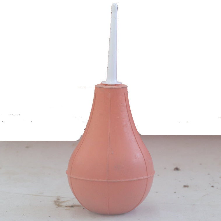 Pink enema bag with a white nozzle on a light wooden surface.