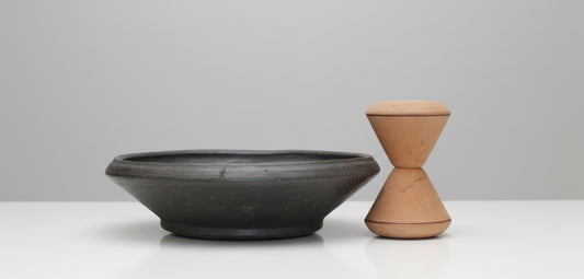Black ceramic bowl and wooden container on a light surface with a blurred background