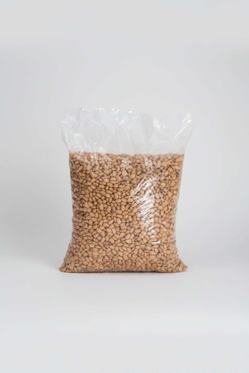 A large clear plastic bag filled with light tan dried beans or lentils, photographed against a plain light gray background.