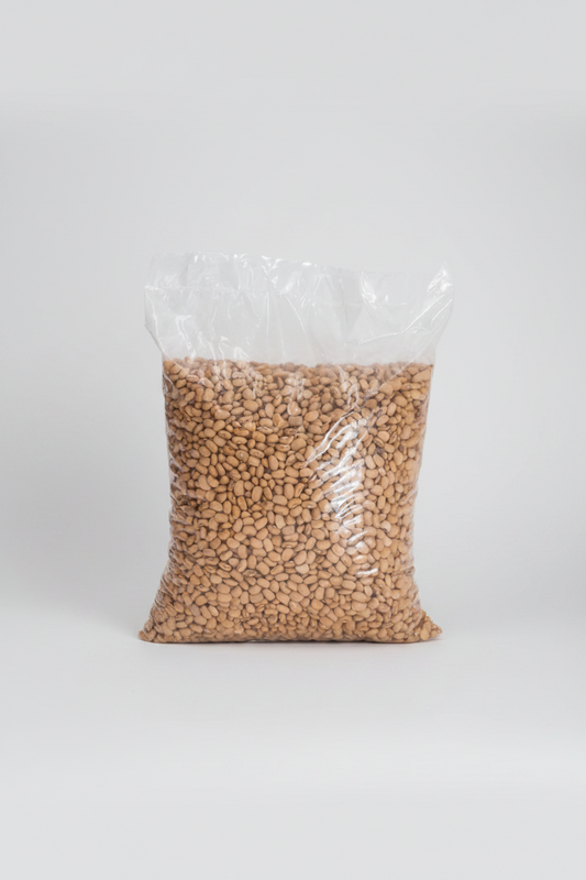 A large clear plastic bag filled with light tan dried beans or lentils, photographed against a plain light gray background.