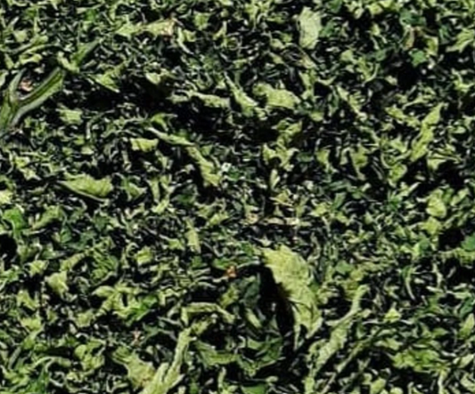 A close-up view of chopped green leafy material, likely herbs, tea leaves, or shredded vegetables, filling the frame.